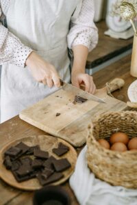 A person chopping chocolate on a wooden board in a cozy kitchen setting, ready for baking.