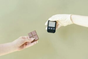 Close-up of hands holding a chocolate bar and glucose meter.